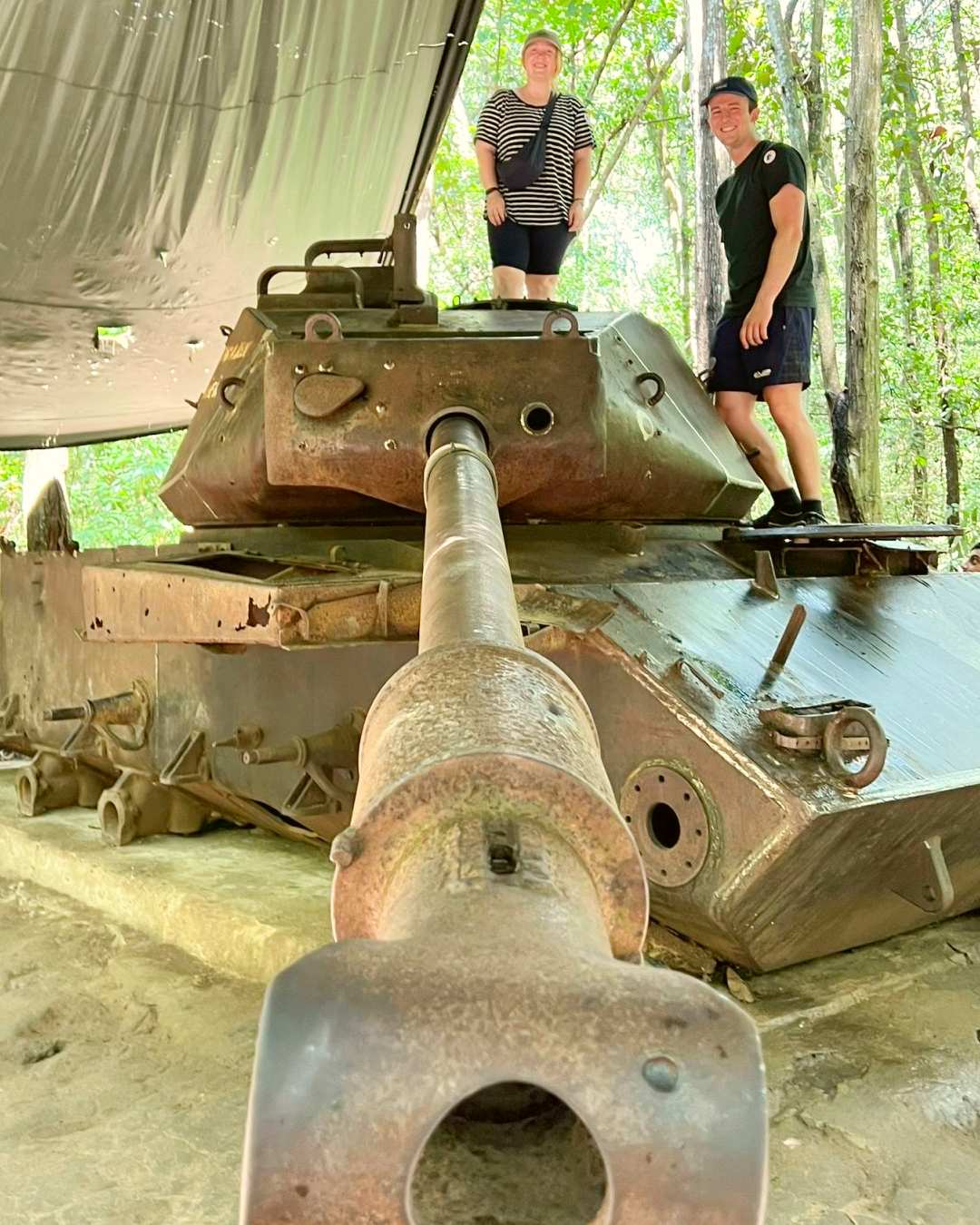 Two travelers standing on a tank on the HCMC history and Cu Chi tour.